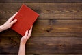 Reading for leasure. Hands take hardback book with empty cover on dark wooden background top view space for text