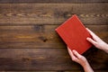 Reading for leasure. Hands take hardback book with empty cover on dark wooden background top view space for text