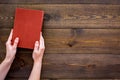 Reading for leasure. Hands take hardback book with empty cover on dark wooden background top view space for text