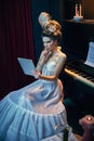 Reading novels. Portrait of young beautiful woman in mage of medieval person in elegant white dress, sitting at piano