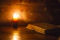 Reading scene in ancient times: an old book leaning on ruined wooden table lighted by a candle on a wooden background