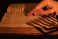Reading Torah. Male hand on old Hebrew Bible in candle light. Shadow from menorah on open Jewish prayer book in the dark