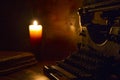 Reading and writing scenes in ancient times: an old book and an old typewriter on a ruined wooden table lit by a candle on a woode