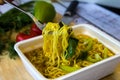 Ready noodles on a fork in the broth with vegetables and green herbs on a wooden board.