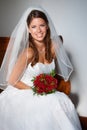 Ready for her nuptials. Portrait of a beautiful young bride sitting on a pew holding a bouquet of roses. Royalty Free Stock Photo