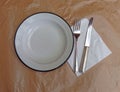 Ready for lunch, white metallic dish, fork and knife on grunge brown paper towel