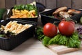 Ready meal to eat in containers with fried chicken wings and raw vegetables on rustic background, cherry tomato and micro greenss