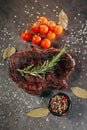 Ready meat steak on a dark metal cutting board, next to a sprig of aromatic rosemary, tomatoes, a black mug with mixed peppercorns Royalty Free Stock Photo