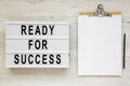 `Ready for success` words on a modern board, clipboard with blank sheet of paper on a white wooden background, top view. Overhea Royalty Free Stock Photo