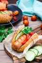 Ready-to-eat appetizing hot dog made from fried sausage, rolls and fresh vegetables, wrapped in parchment paper on a cutting board Royalty Free Stock Photo