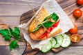 Ready-to-eat appetizing hot dog made from fried sausage, rolls and fresh vegetables, wrapped in parchment paper on a cutting board Royalty Free Stock Photo