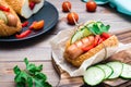 Ready-to-eat appetizing hot dog made from fried sausage, rolls and fresh vegetables, wrapped in parchment paper on a cutting board Royalty Free Stock Photo