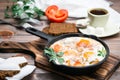 Ready-to-eat breakfast: shakshuka from fried eggs with tomatoes and parsley in a pan, bread with butter and coffeee Royalty Free Stock Photo