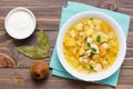 Ready-to-eat chicken soup with potatoes and herbs in a white bowl and sour cream on a wooden table