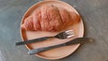 ready-to-eat croissants placed on a brown plate equipped with a fork and knife, on a gray cement table di siang hari