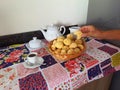 Ready-to-eat homemade cheese breads in a wicker basket on the table set for afternoon coffee. Male hand picking up a cheese bread. Royalty Free Stock Photo