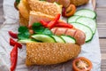 Ready-to-eat hot dogs from fried sausages, sesame buns and fresh vegetables on a cutting board on a wooden table Royalty Free Stock Photo