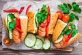 Ready-to-eat hot dogs from fried sausages, sesame buns and fresh vegetables on a cutting board on a wooden table Royalty Free Stock Photo