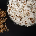 Ready-to-eat popcorn in a glass bowl and corn kernels on a black background. Royalty Free Stock Photo