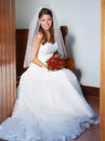 Ready to get married. Portrait of a young bride sitting on a pew holding a bouquet of roses. Royalty Free Stock Photo