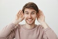 Ready to listen latest gossips. Portrait of handsome excited european man holding palms near ears and smiling with Royalty Free Stock Photo