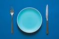 Color plate fork and knife  on blue background. Royalty Free Stock Photo