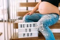 Ready to pop concept - pregnant woman portrait with close up of belly on stairs in home