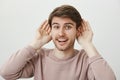 Ready to receive new information. Studio portrait of attractive positive guy holding palms near ears and smiling happily Royalty Free Stock Photo