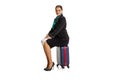 Portrait of pretty young girl, flight attendant, stewardess sitting on suitcase isolated on white studio background.