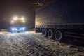 Truck traffic accident at night, on a snowy winter road. Strongly illuminated Wrecker truck pulls a truck out of snow hanging.