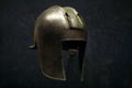 A real antique iron helmet of a Greek warrior decorated with ornaments on a dark background