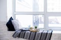 Real apartment interior decor, aromatic candles and plants on vintage tray with pillows and blanket on white windowsill