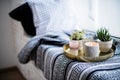 Real apartment interior decor, aromatic candles and plants on vintage tray with pillows and blanket on white windowsill