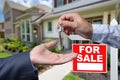 Real Estate Agent Handing Over the House Keys in Front of a Beautiful New Home and For Sale Real Estate Sign. Royalty Free Stock Photo