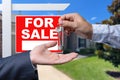 Real Estate Agent Handing Over the House Keys in Front of a Beautiful New Home and For Sale Real Estate Sign. Royalty Free Stock Photo