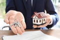 Real estate agent holding house model and keys at table in office Royalty Free Stock Photo
