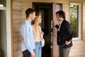 Real estate agent inviting young married couple to enter house for sale