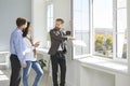 Male realtor shows apartment for sale and its view from window to young married couple. Royalty Free Stock Photo