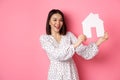 Real estate. Beautiful asian woman demonstrating paper house model, looking at camera confident, advertising home for Royalty Free Stock Photo