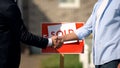 Real estate broker and new house owner shaking hands in front of sold signboard