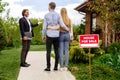 Real estate broker showing house for sale to young couple, outside