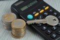 Real estate buying or investing concept with a key resting on a calculator with stacks of coins close up