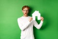 Real estate and buying property concept. Surprised young redhead man showing paper house model and looking amazed Royalty Free Stock Photo