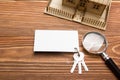 Real Estate Concept. Model house, keys, blank business card, magnifying glass on wooden table. Top view