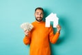 Real estate concept and mortgage concept. Handsome young man buying house, holding home maket and money, thinking and Royalty Free Stock Photo