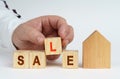 On a white surface there is a model of a house, next to it a man has placed cubes with the inscription - SALE Royalty Free Stock Photo