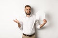 Real estate. Confused man shrugging, showing house paper model and looking indecisive, standing over white background Royalty Free Stock Photo