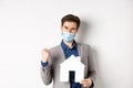 Real estate and covid-19 concept. Excited man in medical mask and suit motivated to buy house, holding paper home cutout Royalty Free Stock Photo