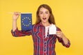 Real estate in EU. Portrait of amazed ginger girl in checkered shirt holding European flag and paper house, looking at camera with