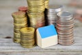 Real estate investment concept with small model house with blue roof surrounded by piles of money Royalty Free Stock Photo